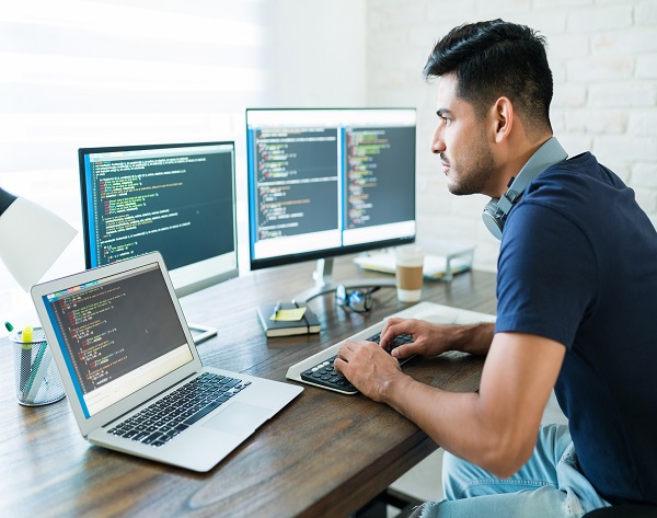 Side view of attractive Hispanic software developer programming using computer while working from home